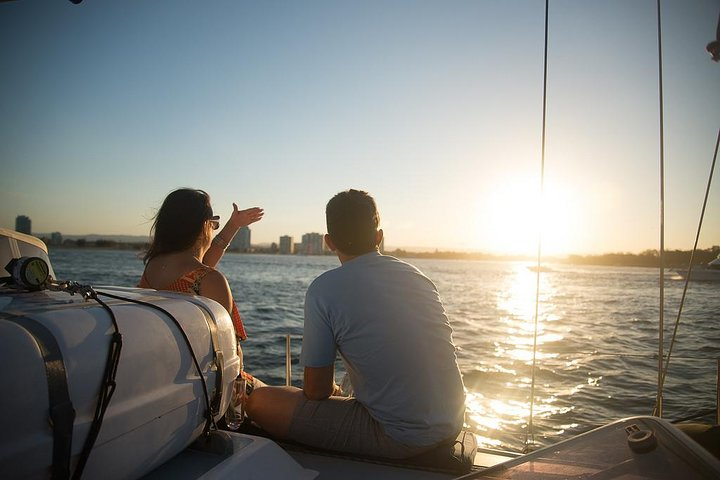 Savor the moment as the sun dips below the horizon enjoying sparkling wine and nibbles while cruising the serene Gold Coast waters with friends creating lasting memories against a stunning backdrop.
