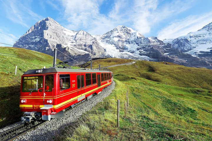 Journey through the Swiss Alps aboard a cogwheel train surrounded by imposing peaks and lush meadows heading towards the iconic Jungfraujoch the highest railway station in Europe.