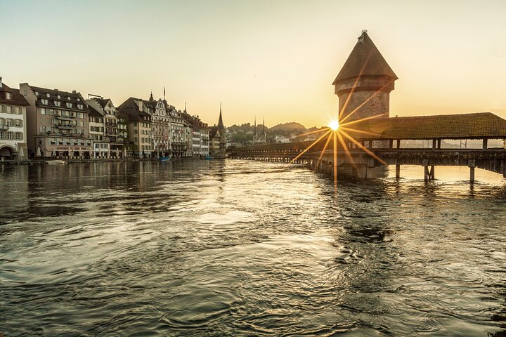 Experience the serene beauty of Lake Lucerne as the sun sets over the iconic Chapel Bridge inviting exploration of captivating medieval streets and culinary delights in Lucerne's charming Old Town.