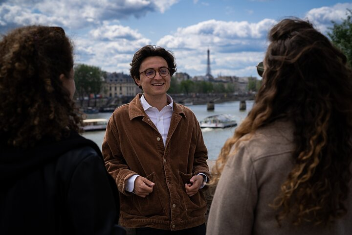 guy with glasses smiling in front of 2 woman with a bridge and eiffel tower in the background