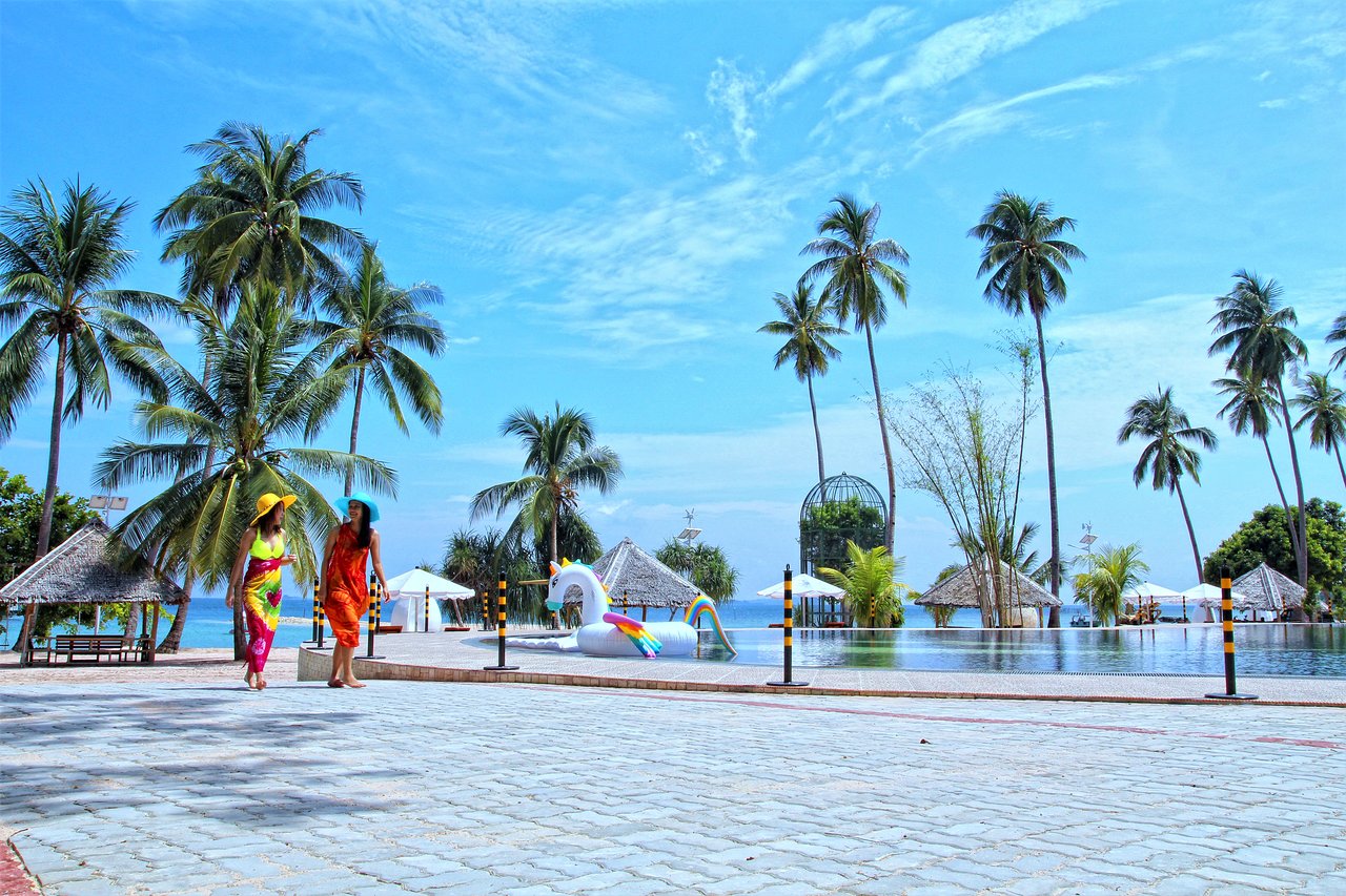 Palm-fringed pathways lead to a serene pool inviting relaxation under the sun. Discover picturesque views and the essence of island life at Kepri Coral Resort Batam.