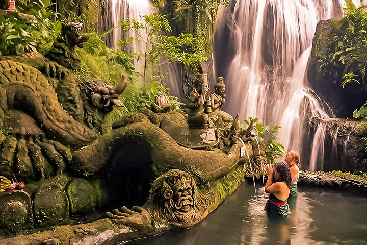 Immerse yourself in the tranquility of Gria Beji Waterfall surrounded by lush greenery and ancient sculptures as you partake in a serene purification ceremony in Bali.
