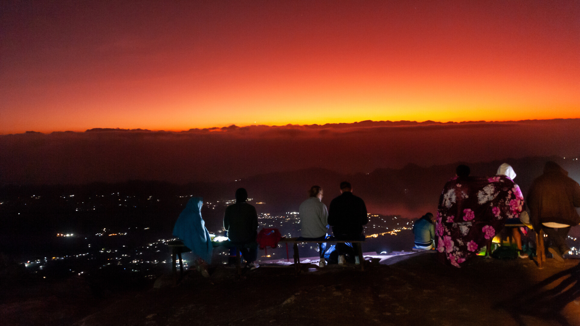 Witness the breathtaking transformation of the sky as dawn breaks over Bali with stunning colors illuminating the landscape and fellow adventurers enjoying the tranquility at Mount Batur's summit.