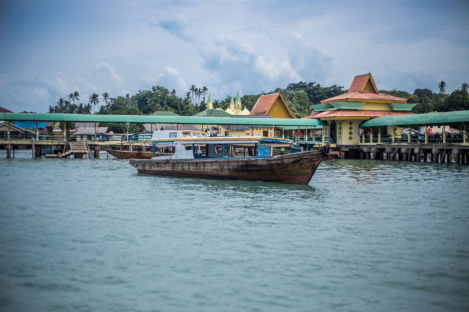 Explore the tranquil waters as a traditional boat glides by colorful waterfront villages inviting travelers to uncover the rich history of Penyengat Island's royal past and scenic charm.