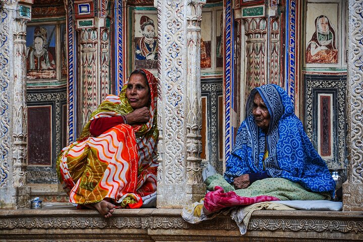 Women dressed in traditional sari sitting in front of haveli in Mandawa.