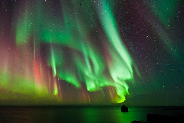 Experience the magic of Iceland’s night sky as the Northern Lights dance above serene waters. Enjoy cozy blankets homemade treats and expert guidance on this unforgettable adventure.