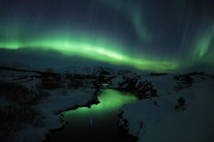 Experience the dance of the Northern Lights over Iceland's serene landscapes as a guided adventure leads you to enchanting views and unforgettable moments under the starry sky.
