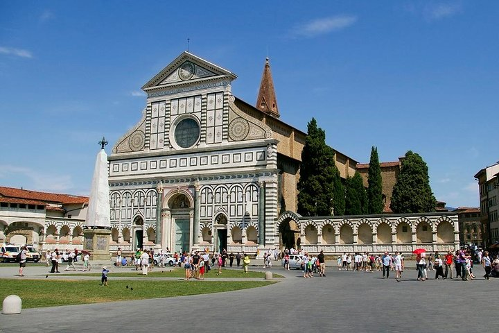 Explore the stunning Renaissance façade of Santa Maria Novella Basilica surrounded by lush greenery and lively visitors offering a perfect blend of history and beauty in Florence.