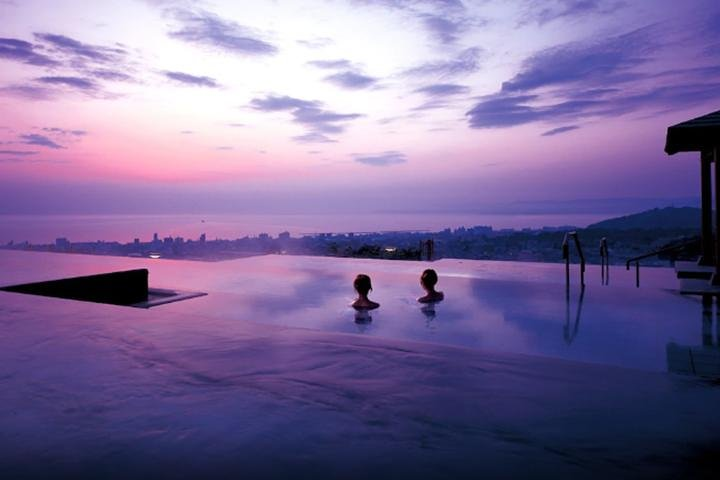Relax in a serene hot spring surrounded by breathtaking views of nature as the sun sets creating a perfect backdrop for a rejuvenating escape in Beppu.
