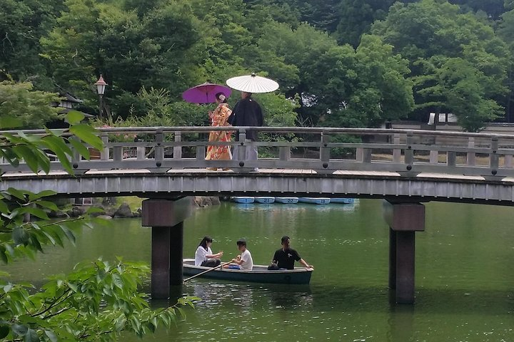 Enjoy a serene stroll across a quaint bridge surrounded by lush greenery while traditional boat rides glide beneath highlighting the beauty of Osaka’s historical charm and natural splendor.
