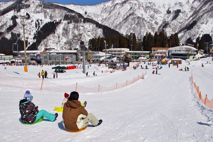 Experience the joy of snow sledding in picturesque scenery surrounded by majestic mountains and fellow adventurers creating unforgettable memories in the winter wonderland of Tokyo.