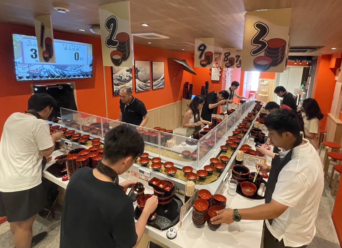 Experience the joy of Wanko Soba as guests eagerly enjoy endless noodles surrounded by fellow food enthusiasts with fun condiments adding to the unique dining adventure.