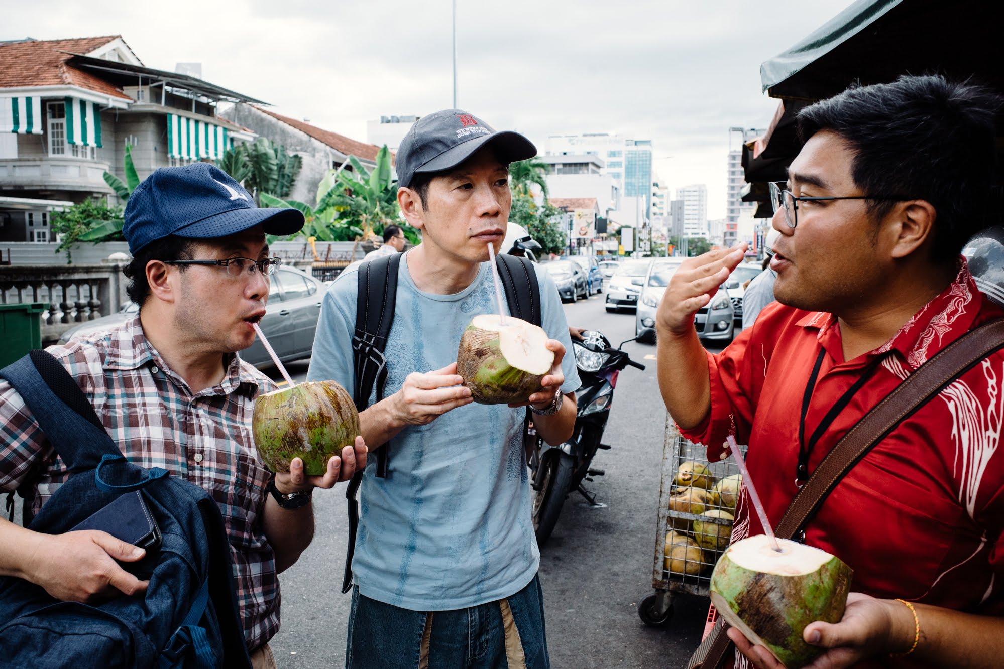 Savor the unique local flavors as travelers share laughs over fresh coconuts immersing themselves in Penang's rich food culture and daily rituals of street dining.