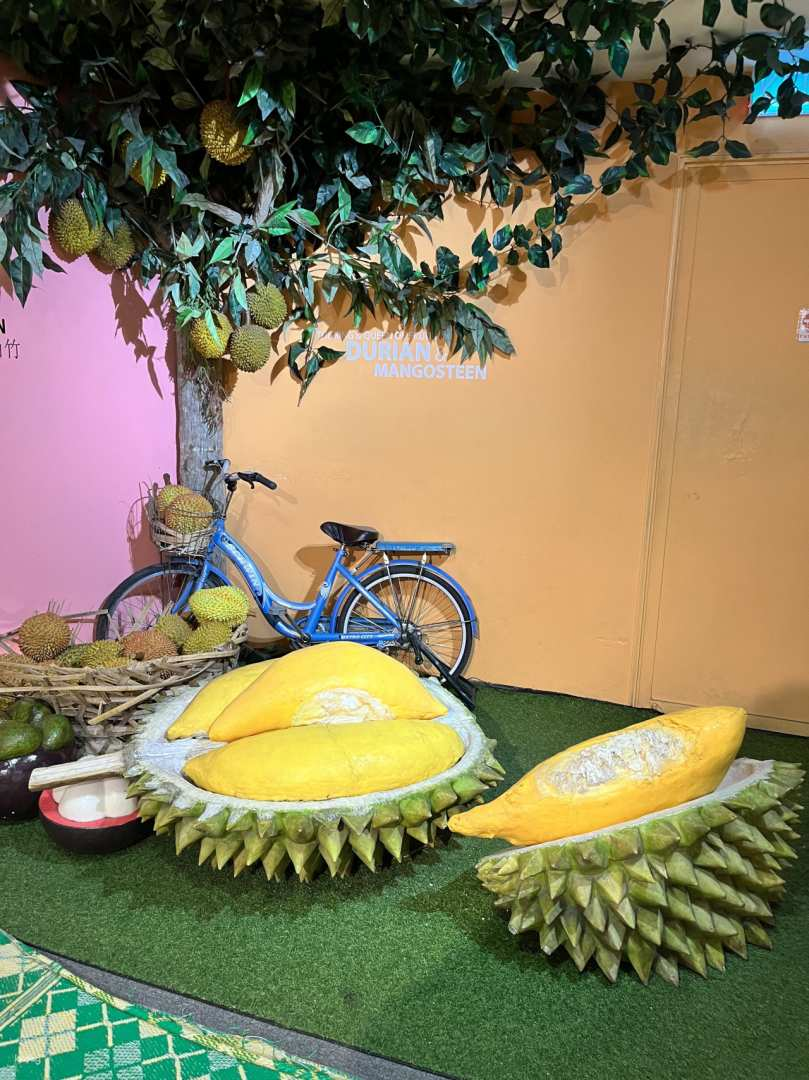 Step into a whimsical world showcasing Malaysia's culinary delights featuring oversized fruits and charming decor that invites playful exploration and memorable photos. Perfect for food lovers and travelers alike.