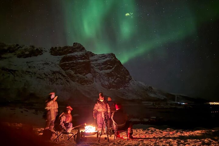 Experience the magic of the northern lights while enjoying hot food and drinks around a cozy bonfire surrounded by breathtaking Arctic landscapes of snow-capped mountains and serene fjords.