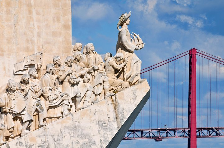 Explore Lisbon's rich history and culture at the Padrão dos Descobrimentos a tribute to Portugal's explorers with the iconic red bridge framing this monumental scene.