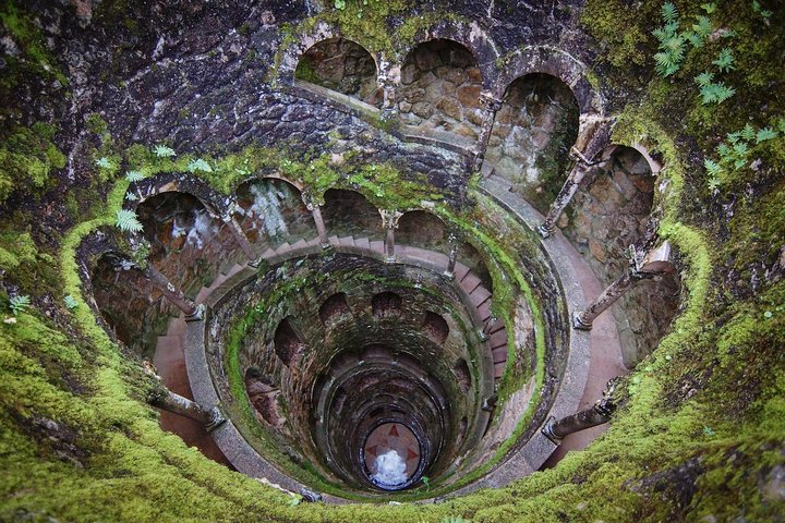 Discover the mystical allure of Quinta da Regaleira's Initiation Well where spiraling stone steps and lush greenery create a surreal journey into a hidden world of wonder.