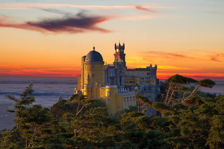 Experience the charm of Sintra as the sun sets behind the stunning Pena Palace surrounded by lush greenery and breathtaking views of the Atlantic Coast and beyond.