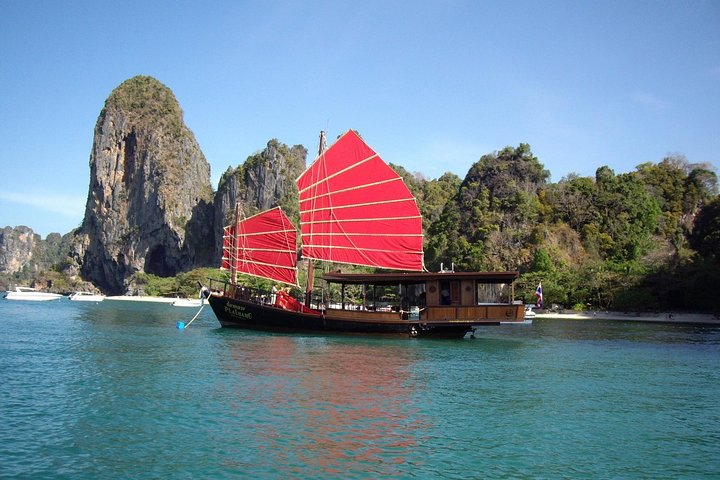 Sail through crystal-clear waters aboard a charming wooden junk exploring stunning limestone formations and enjoying the serenity of Krabi's coastline perfect for memorable adventures.