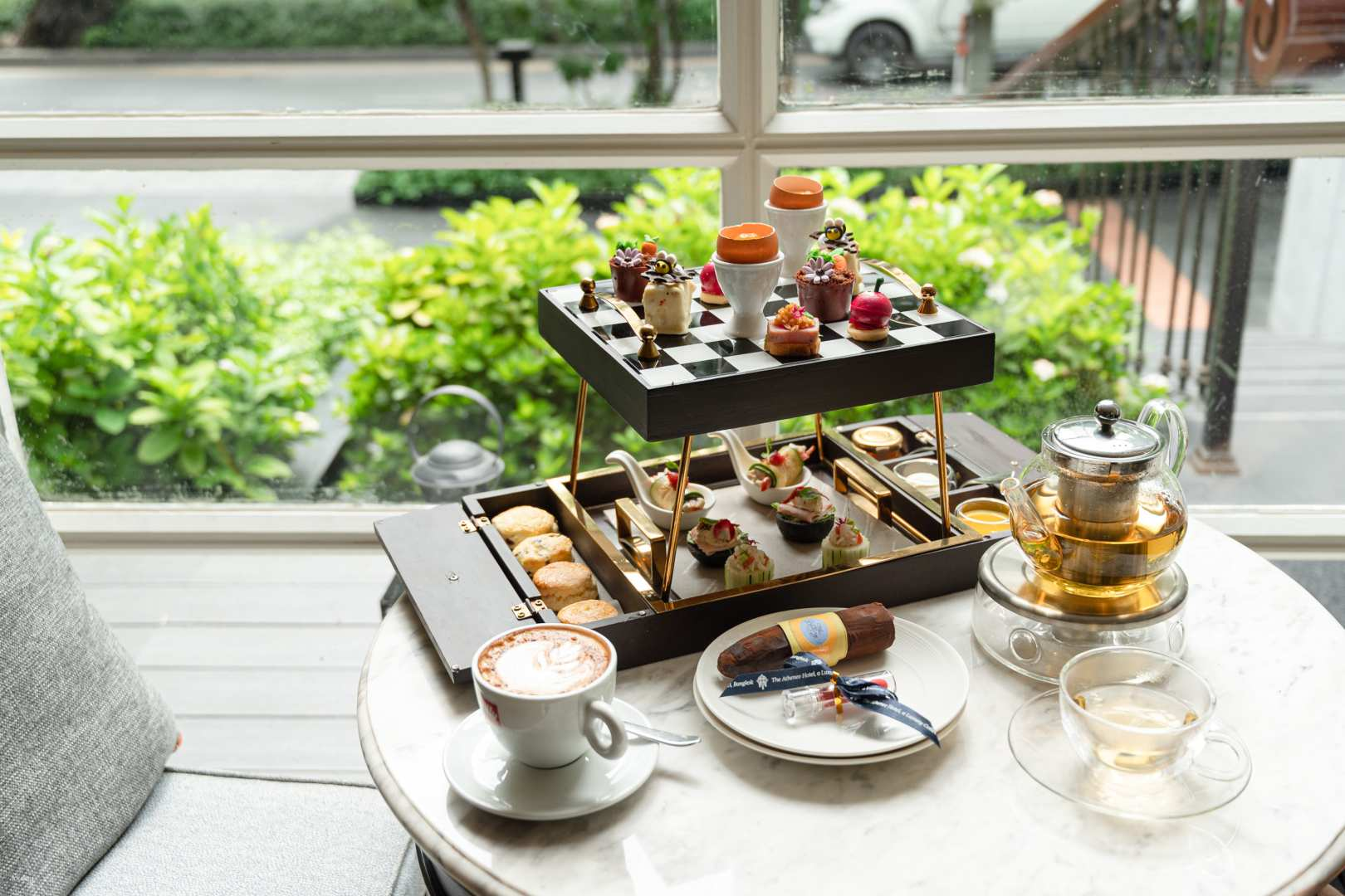 Experience a serene tea time at The Bakery in The Athenee Hotel Bangkok with exquisite Thai-French pastries and a scenic view of lush greenery perfect for a relaxing afternoon.