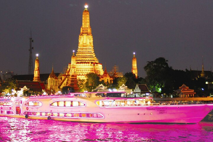 Savor authentic Thai cuisine while cruising along the Chao Phraya River taking in stunning views of illuminated landmarks like Wat Arun against the night sky.