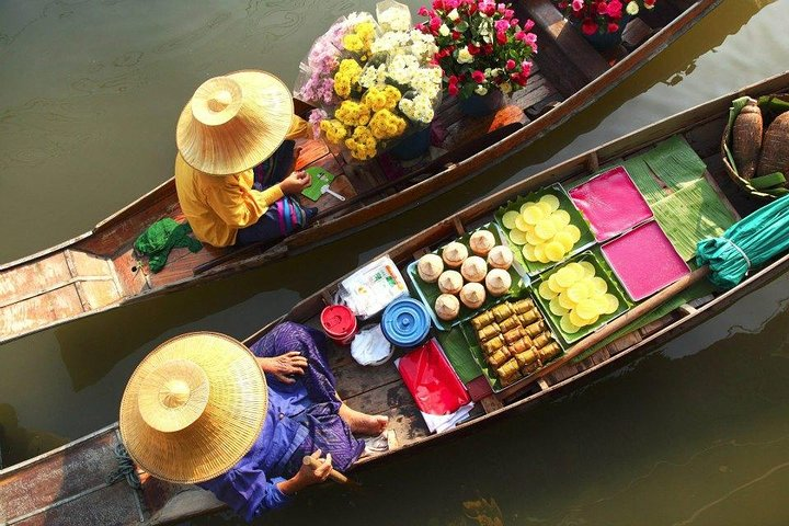 Experience the charm of Damnern Saduak Floating Market with colorful boats showcasing fresh produce and vibrant flowers immersing travelers in a unique local shopping tradition.