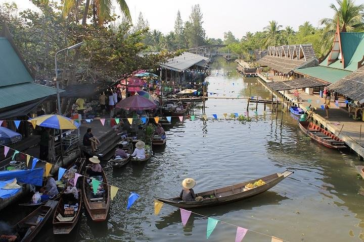 Experience the charm of Tha Kha Floating Market where traditional wooden boats glide along serene waters offering a glimpse into authentic Thai local life amidst lush greenery and colorful stalls.
