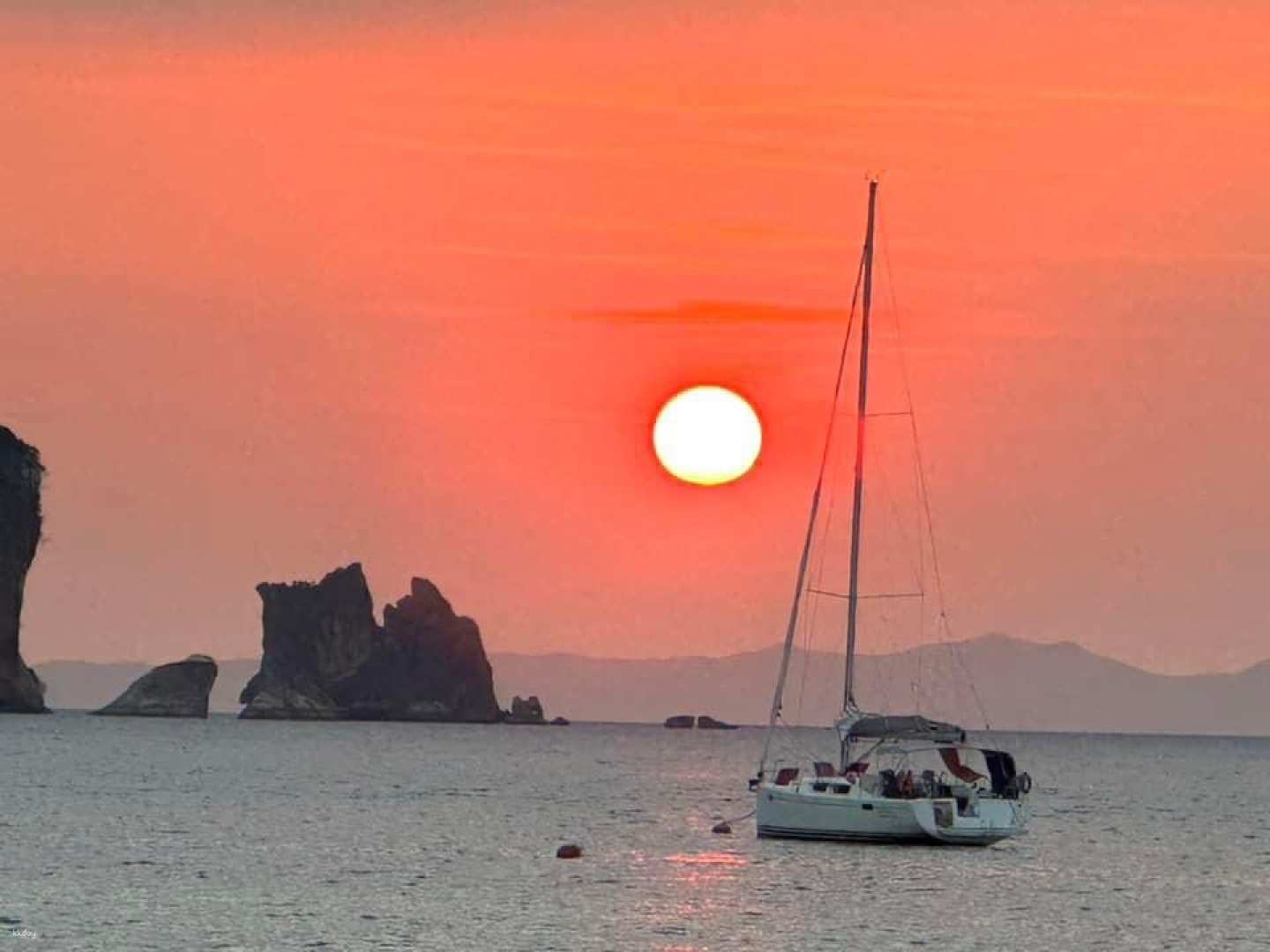 Experience the beauty of a sunset over the sea where a sailboat glides past stunning rock formations capturing the essence of a perfect day in Thailand's picturesque islands.