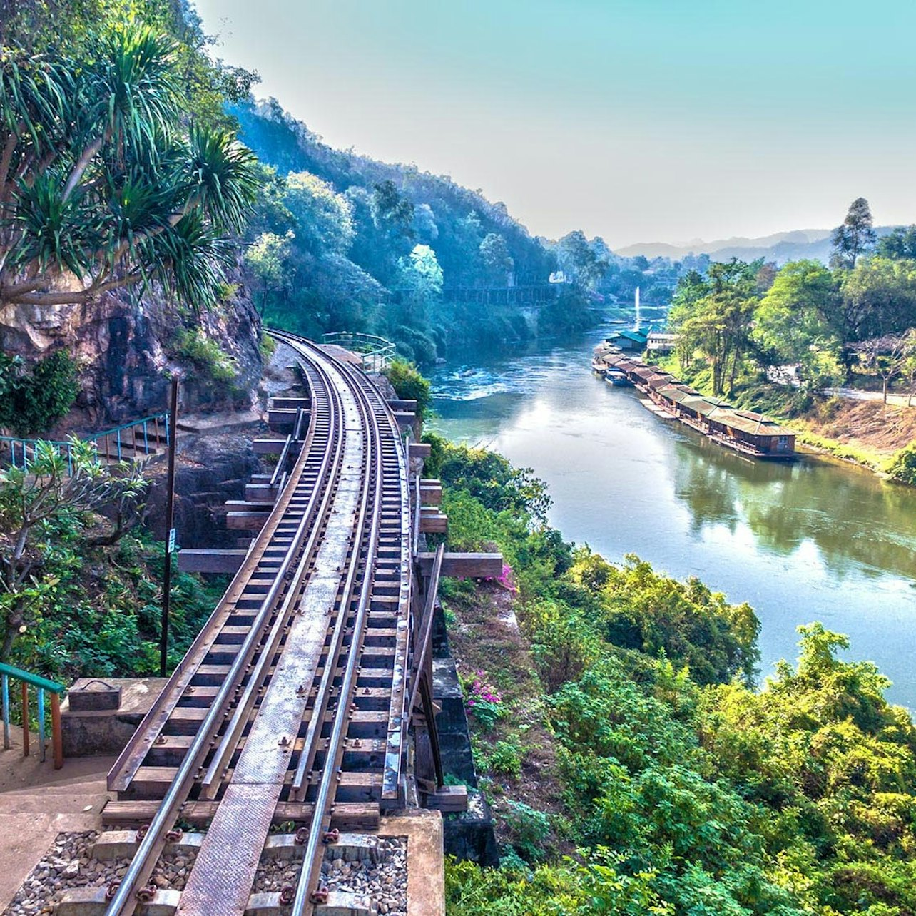 Explore the serene beauty of the River Kwai with its historic railway alongside lush hills offering a glimpse into the past and a peaceful escape into nature's embrace.