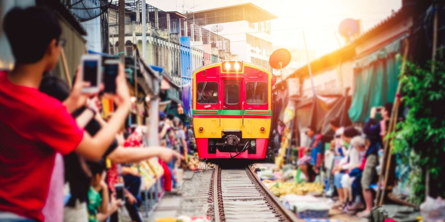 Experience the unique charm of Maeklong Railway Market as the train approaches prompting stalls to retract and creating a dynamic scene filled with local vendors and excited onlookers.