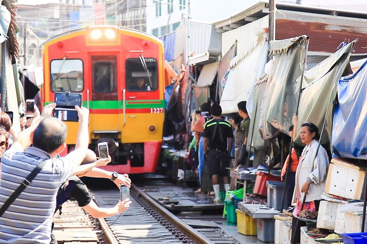 Experience the unique sight of a train weaving through bustling market stalls where vendors quickly fold their awnings illustrating the charming blend of everyday life and local commerce.