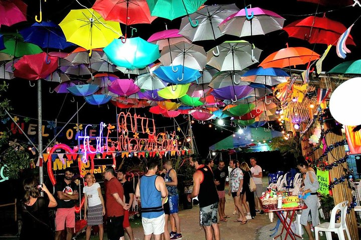 Experience the lively charm of Hat Rin Beach illuminated by colorful umbrellas and bustling with partygoers. Join fellow travelers for an unforgettable night under the stars with convenient round-trip transfers.
