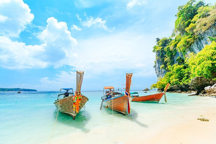 Explore the serene waters of Phuket where traditional long-tail boats rest along pristine shores surrounded by lush greenery and stunning cliffs inviting travelers to unwind and savor the beauty of Thailand.