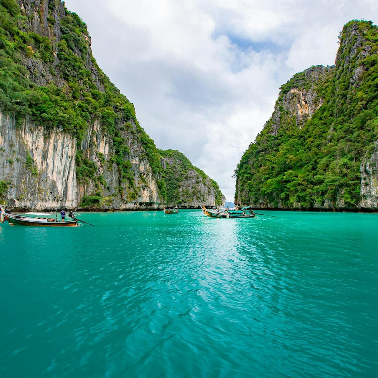 Explore the stunning turquoise waters between soaring cliffs on a longtail boat perfect for snorkeling and discovering the beauty of Phi Phi Islands including secluded beaches and rich marine life.