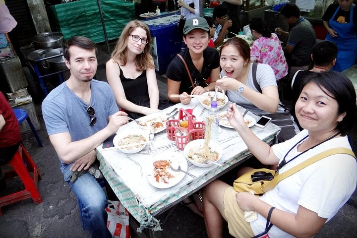Dive into the culinary treasures of Thonburi as you share delightful dishes with friends savoring authentic flavors and connecting with local food culture in a bustling street setting.
