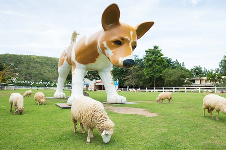 A giant dog statue watches over playful sheep in a lush green landscape creating a unique blend of quirky charm and serene nature perfect for memorable photos and leisurely strolls.