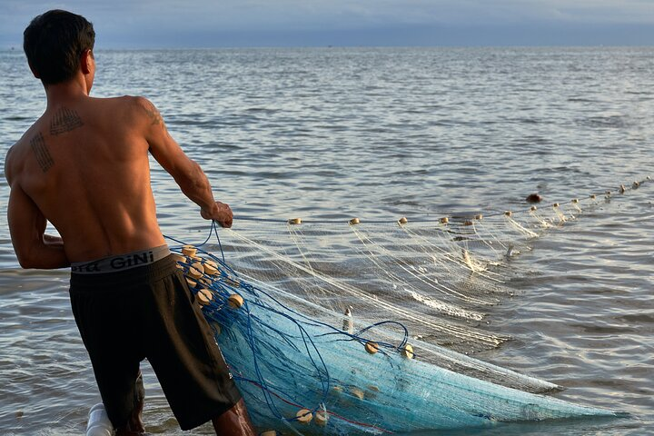 Experience the tranquil charm of local fishing traditions as you witness fishermen at work casting nets into the serene waters surrounded by the beauty of nature and rich cultural heritage.