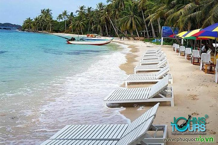 Experience the serene beauty of Phu Quoc’s beaches unwind on comfortable loungers and soak in the sun as boats glide across crystal-clear waters inviting adventure and relaxation.